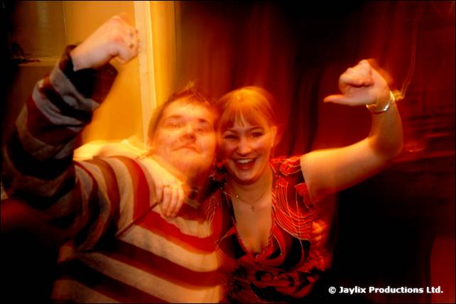 A man in a striped top and a woman in a patterned top raise their arms, smiling