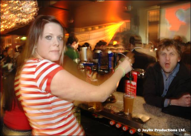 A woman in a red and white striped top pulls a pint at the bar, with a man behind her pulling a face