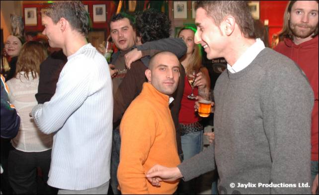 A group of people stand talking and drinking in a busy bar