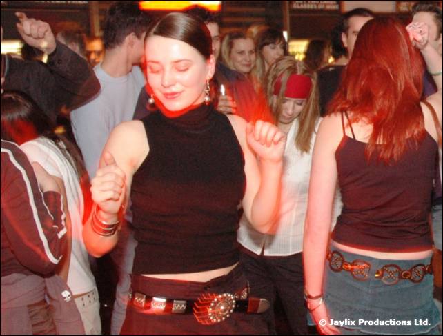 A woman in a black halter top dances with her eyes closed among other dancers