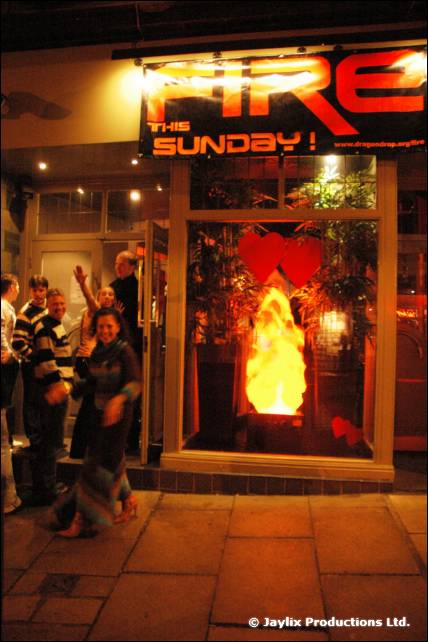 A FIRE This Sunday sign above a shop window with a flame display, and people outside at night