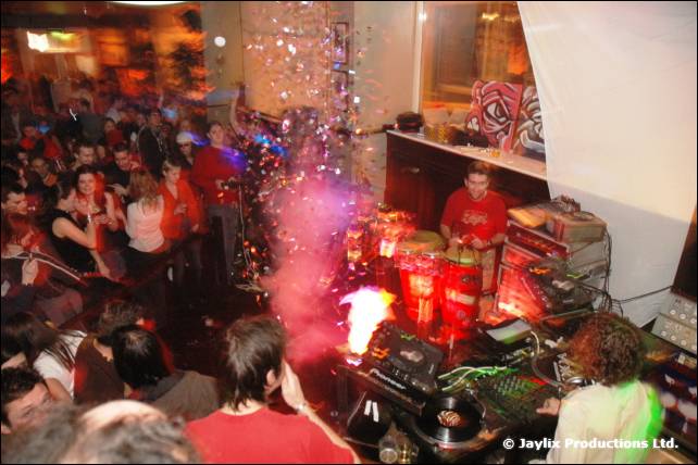 A DJ at decks behind a crowd, with sparks, red light and tinsel in the air