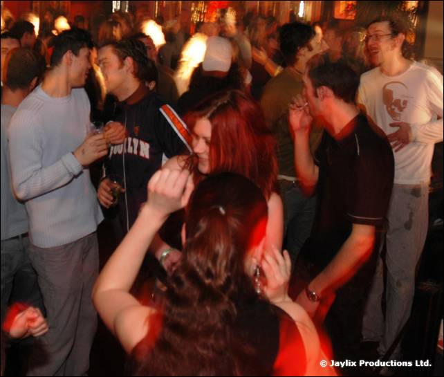 Dancers in a crowded bar, with several people in the foreground moving and blurred