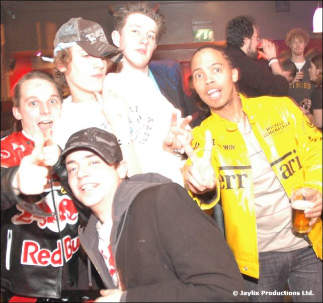 A group of young men pose and point at the camera, one in a yellow jacket and one in a Red Bull jacket