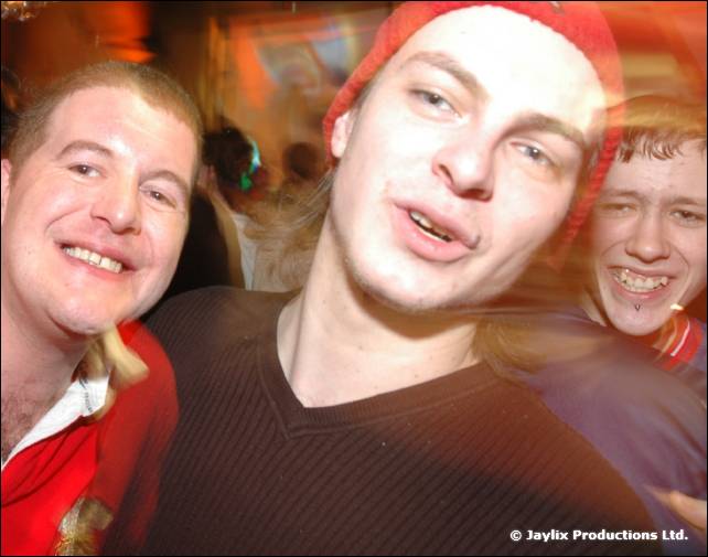 Three people crowd the camera with big smiles, one wearing a red woolly hat, blurred with motion