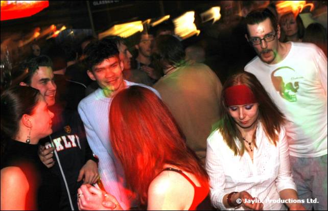 A busy dance floor with people in motion, one wearing a red headband and another in glasses and a white shirt