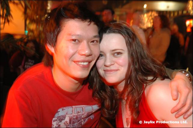 A man and a woman in red tops smile close together in a warmly lit bar