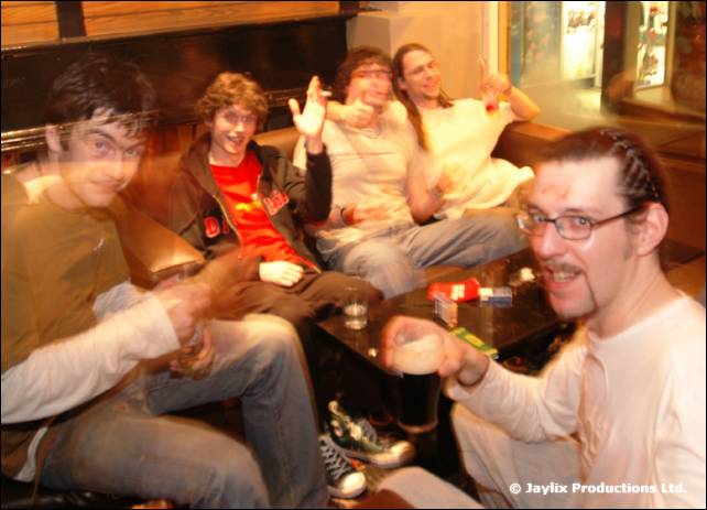 Five people sit on bench seating at a table, several smiling and gesturing at the camera