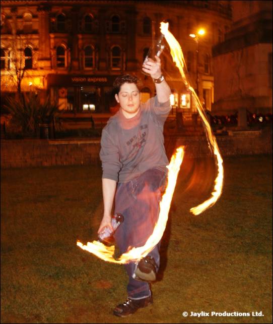 A person spins a burning rope outdoors at night in front of a stone building