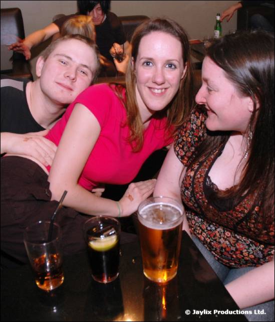 Two women and a man sit together at a table with a pint of beer and two other drinks