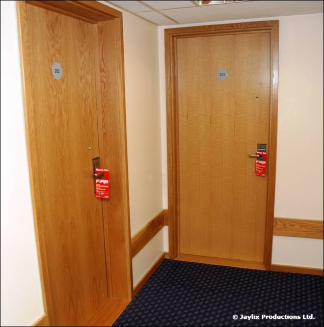 A hotel corridor with two wooden doors, each with a red FIRE door hanger on the handle