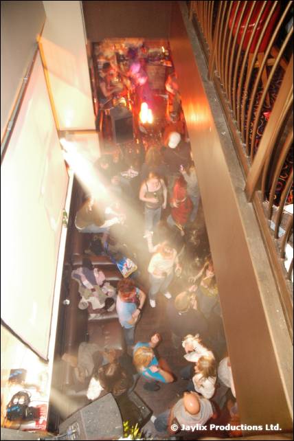 A view down from a balcony onto people in a bar, with a shaft of light across the room