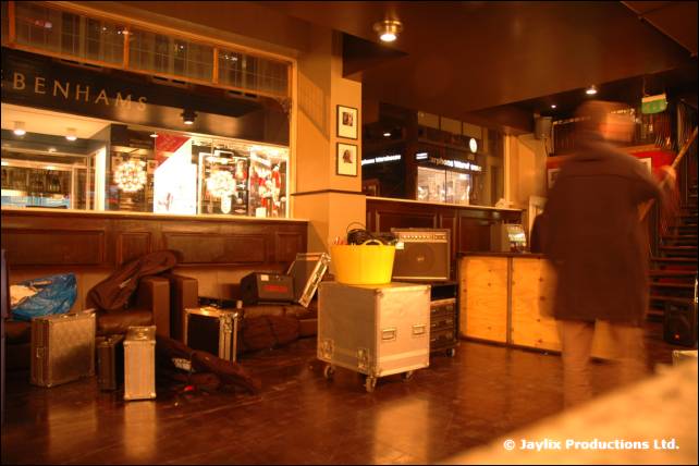 A blurred person walks past flight cases and a yellow tub in a bar lounge