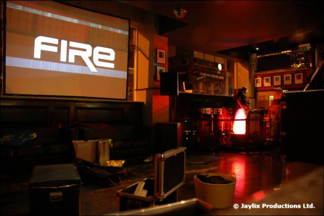 A projector screen showing the FIRE logo in a dark bar, with drums and a red glow behind