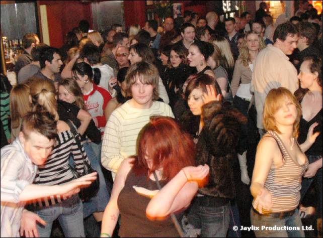 A packed dance floor with people dancing, a woman with red hair in the foreground