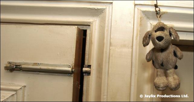A soft toy dog hangs from a door frame beside a latch