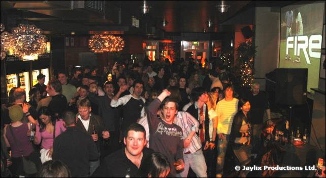 A crowded bar with a FIRE logo on a screen at the top right