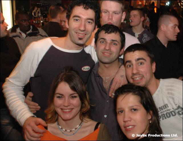 A group of men and women pose together in a crowded bar, smiling at the camera