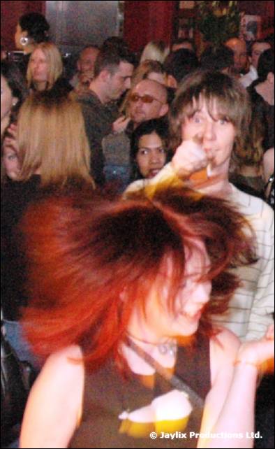 A woman with red hair tosses her head in the foreground of a packed crowd