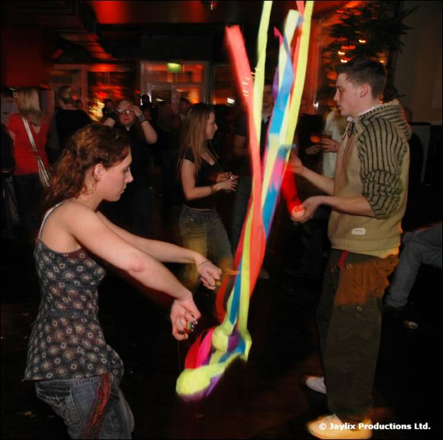 A woman dances while a man in a striped waistcoat swings long coloured ribbons