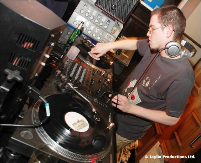 A DJ in glasses and headphones mixes on turntables, seen from above