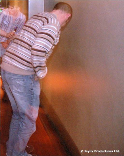 A person in a striped jumper and jeans leans forward beside a wall, slightly blurred