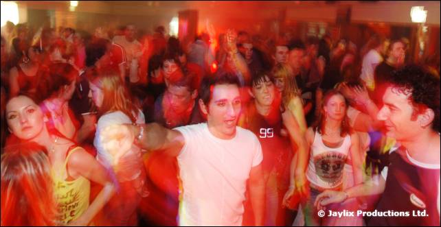 A crowd dances close together, a man in a white t-shirt at the centre