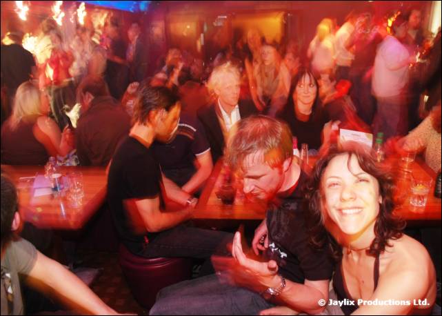 A packed bar with people seated at tables, a smiling woman in the foreground
