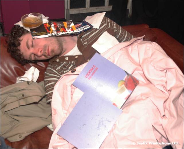 A man sleeps on a leather sofa with a glass on his chest and a cocktail menu nearby