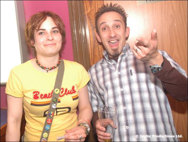 A woman in a yellow Beach Club t-shirt stands beside a man in a check shirt pointing at the camera