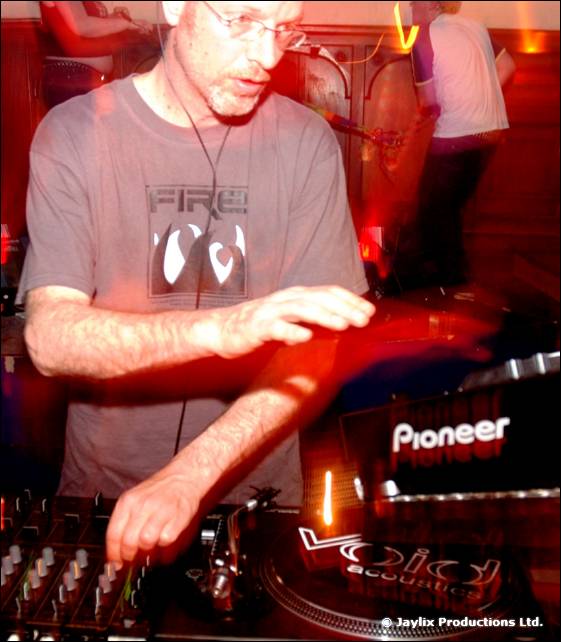 A man in glasses and a grey FIRE t-shirt plays records on Pioneer decks