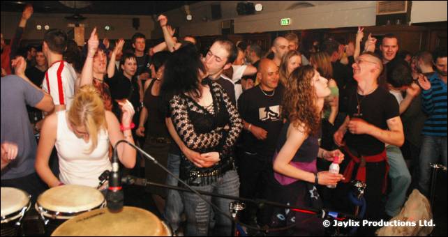 A crowd dances next to bongo drums and a microphone