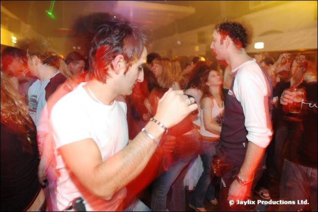Two men dance in a crowd, one in a white t-shirt and one in a dark top with white sleeves