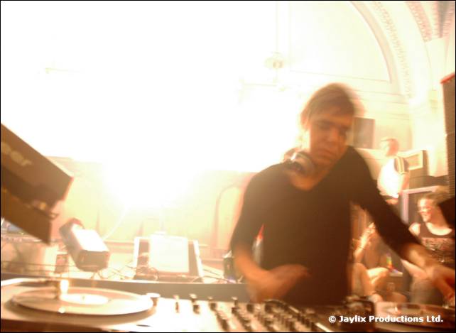 A DJ in a dark top plays at turntables in bright overexposed light