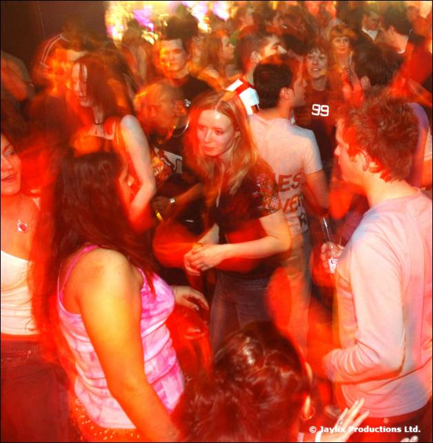 A crowd dances in red light, one person wearing a number 99 top