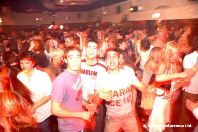 A crowd faces the camera in a large hall, men in front in pink and white t-shirts