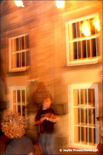A blurred person stands in front of a stone building with lit windows at night