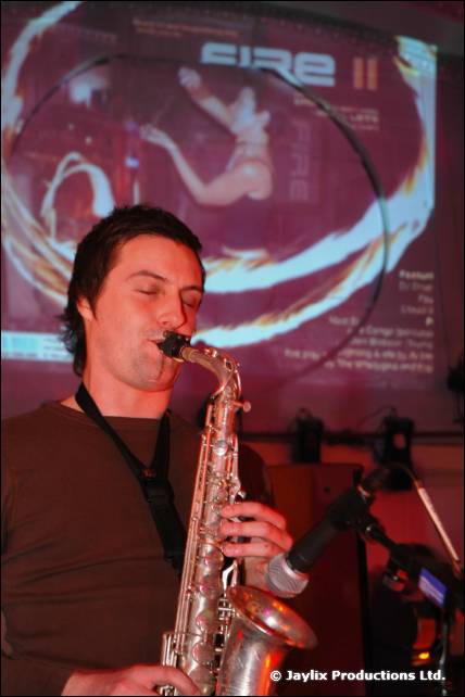A man plays a saxophone in front of a projected FIRE II flyer