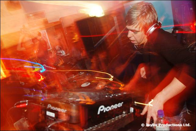 A DJ wearing headphones works at Pioneer decks, with streaks of light