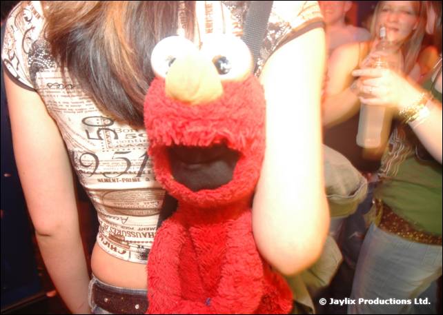 A red Elmo soft toy is held in front of a person in a patterned top