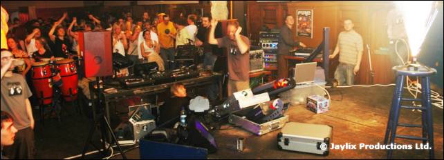 A wide view of a stage with DJ equipment, congas, and a crowd at the back