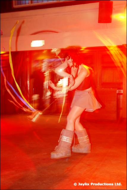 A person in white boots and a short skirt swings ribbons in blurred red light