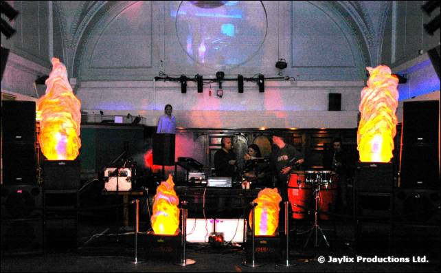 A stage with drums and speakers, lit flame shaped lights on stands and a circular projection behind