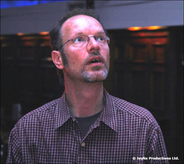 A bespectacled man with a beard in a check shirt looks upwards