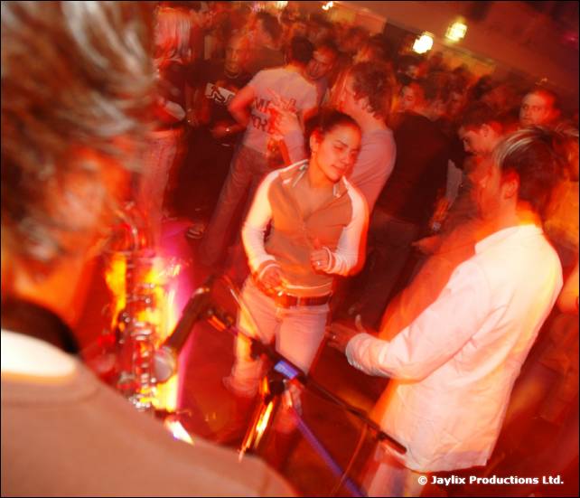 People dance in blurred red light, a woman in the centre and a man in white on the right
