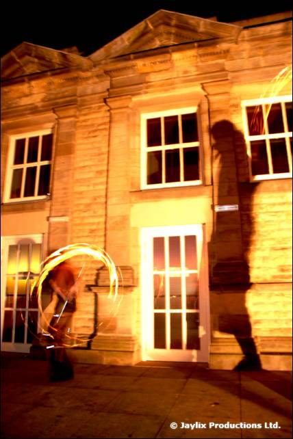 A stone building lit at night with a faint ring of light trails on the left