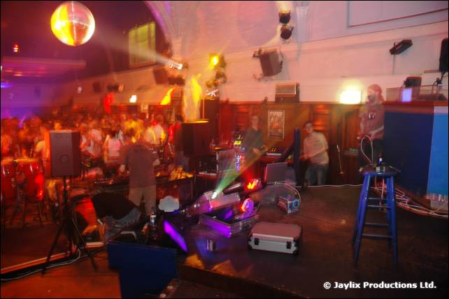 A hall with a mirror ball, a stage, flight cases and a blue stool, with people at the back