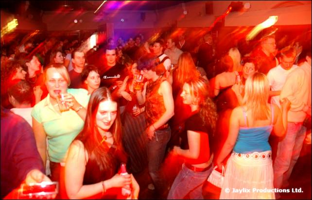 A crowd dances in red light, a woman in a green top in the front