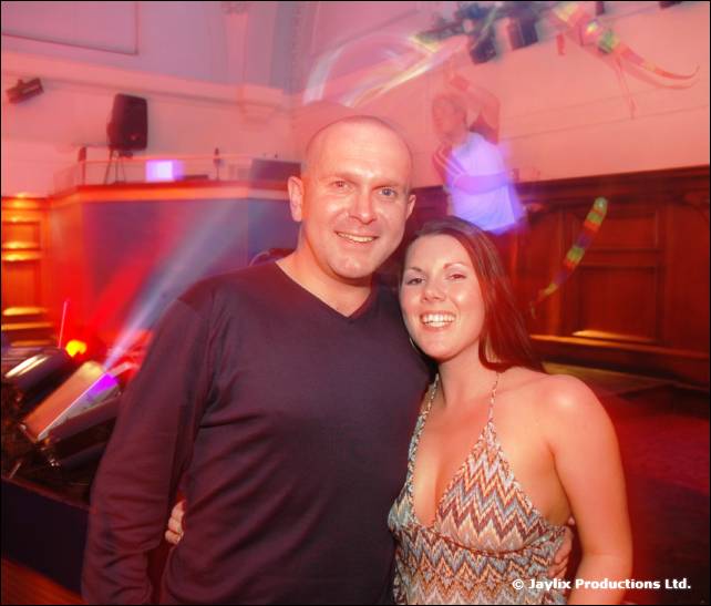 A man and a woman pose together in a hall with coloured lights