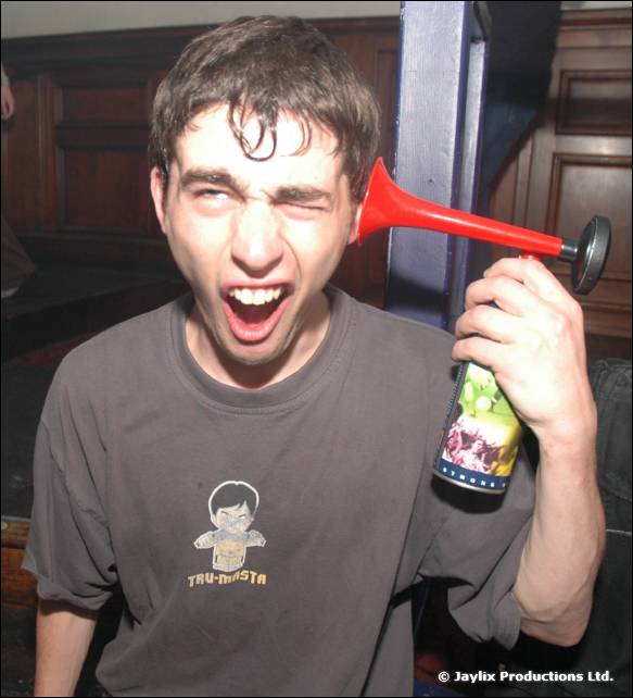 A man in a grey t-shirt grimaces and holds an air horn and a bottle